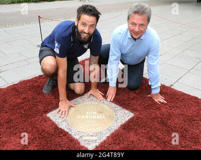 23. Juni 2021, Sachsen-Anhalt, Magdeburg: Bennett Wiegert (l), Trainer des Handball-Bundesligisten SC Magdeburg, und Lutz Trümper, Oberbürgermeister von Magdeburg, hocken vor der Granitbronze-Skulptur 'Sports Walk of Fame', die die EHF-Europameister des SC Magdeburg heute enthüllen durften. Der SC Magdeburg hatte im Mai den Titel der EHF-Europaliga geholt. Die in den Bordstein eingebettete und dem „Walk of Fame“ in Hollywood nachempfundene Plakette soll diesen Erfolg und viele andere sportliche Spitzenleistungen der Handball-Bundesliga würdigen. Der „Sports Walk of Fame“, whi Stockfoto