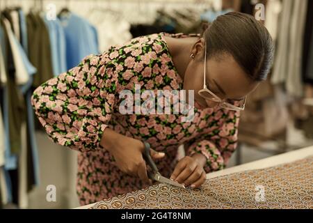 Afrikanische weibliche Modedesignerin schneidet Material auf einer Studio-Werkbank Stockfoto
