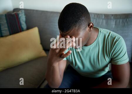 Junger afrikanischer Mann, der auf seinem Sofa sitzt und verzweifelt aussieht Stockfoto