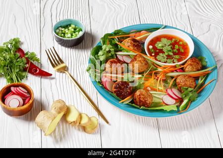 Vietnamesischer Banh-mi-Salat mit Fleischbällchen, Karotten, Gurken und Rettich, serviert über Salat mit Rosenkohm auf einem blauen Teller mit süßer Chilisauce Stockfoto