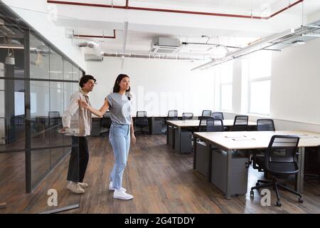 Lässig gekleideter junger Mann und Frau auf der Suche nach Räumlichkeiten für ein Startup-Unternehmen, die in ein leeres, modernes Großraumbüro gehen Stockfoto
