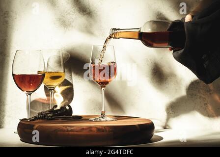 Weinprobe. Roséwein, der auf dem Hintergrund in ein Glas gegossen wird, mit einer Auswahl an Rot-, Weiß- und Roséweinen in Gläsern. Hartes Sonnenlicht und Schatten von Foliag Stockfoto