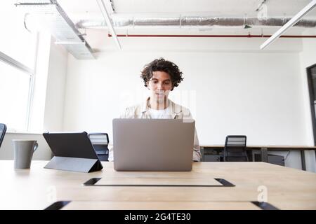 Lässig gekleideter junger Mann, der in einem modernen Großraumbüro am Schreibtisch auf einem Laptop arbeitet Stockfoto