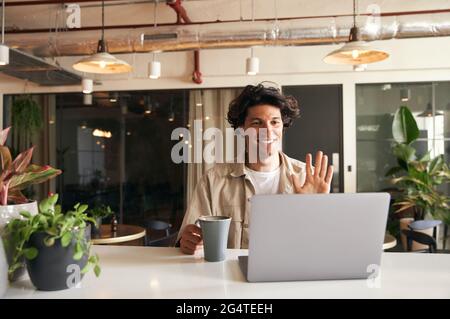 Ein junger Mann, der per Videoanruf am Laptop am Tisch im Café arbeitet und virtuelle Meetings veranstaltet Stockfoto