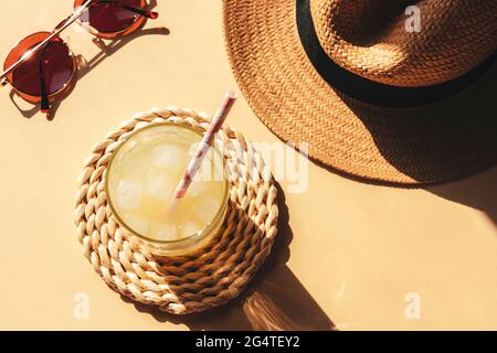 Ein Glas mit Limonade und Strandzubehör auf gelbem Hintergrund mit harten Schatten, Draufsicht. Stockfoto