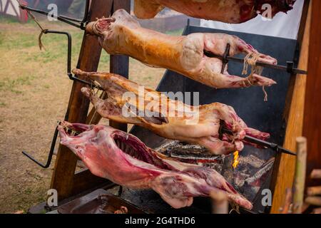 Prozess des Kochens von Schweinefleischkadavern am Spieß auf dem sommerlichen Lebensmittelmarkt Stockfoto