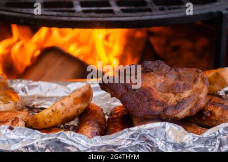 Prozess des Kochens von Steaks, Würstchen und Kartoffeln in Folie auf dem Brazier Stockfoto