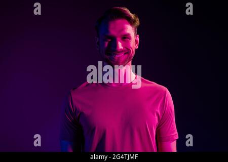 Portrait von attraktiven fröhlichen Inhalt Kerl im Nachtclub isoliert über dunklen Neon Licht violetten Hintergrund Stockfoto