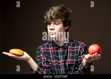 Junger Mann hält und wählt zwischen Apfel oder Hamburger Stockfoto