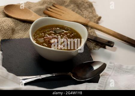 Linsenplatte mit Kartoffeln, Lauch und für Spanien typischen Chorizo auf einem schwarzen Schiefertablett mit traditionellem Holzbesteck mit selektivem Fokus. Stockfoto