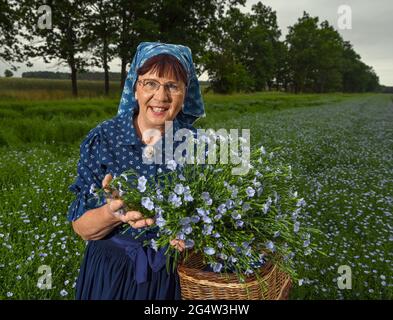 22. Juni 2021, Brandenburg, Dürrenhofe: Gisela Christl (Spreewald Christl) steht in sorbisch-wendischem Arbeitskostüm am Rande einer Pressekonferenz zur Ölflachsblüte auf einem Feld der Landwirtschaftsgenossenschaft Unterspreewald z.B. mit blühendem Ölflachs. Flachs, aus dem die Müller das Spreewald-Leinöl pressen, wächst auf rund 160 Hektar Ackerland im Spreewald. Aufgrund des warmen Wetters beginnen die Flachskulturen derzeit zu blühen. Der Leinsamen ist eine traditionelle Kultur des Spreewaldes. Die Produktion von Leinöl ist seit Generationen in der Region verwurzelt. Stockfoto