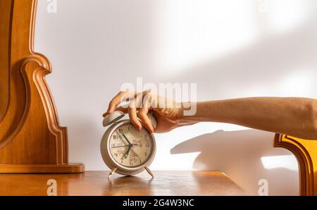 Erschöpfte, müde Person schaltet am Morgen den weißen Wecker aus Stockfoto