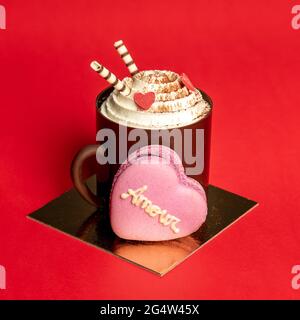 Essbare Schokoladenbecher mit heißem Kaffee, Schlagsahne und herzförmigem Macaron auf roter Oberfläche Stockfoto