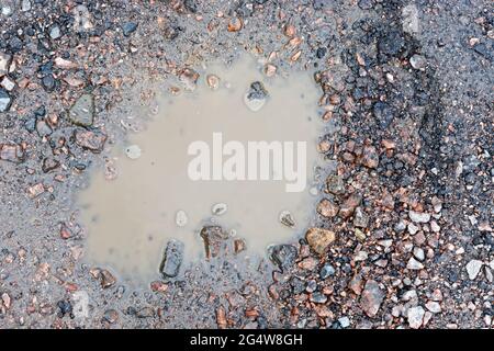 Draufsicht auf eine kleine Pfütze mit schlammigem Wasser auf einer felsigen Landstraße. Stockfoto