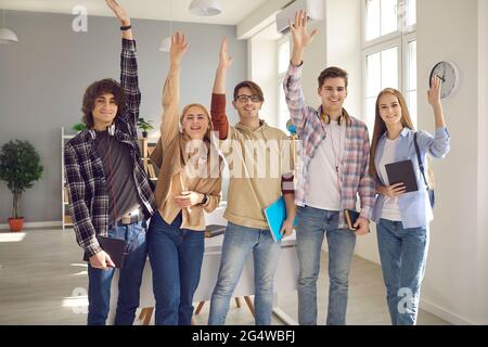 Eine Gruppe glücklicher intelligenter Schüler, die im Klassenzimmer stehen und die Hände zusammenheben Stockfoto