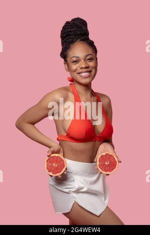Dunkelhäutige Frau, die Grapefruitscheiben hält und glücklich aussieht Stockfoto