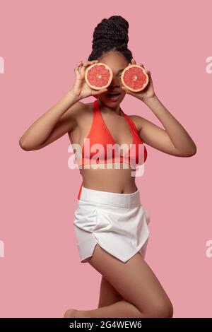 Dunkelhäutige Frau, die Grapefruitscheiben hält und glücklich aussieht Stockfoto