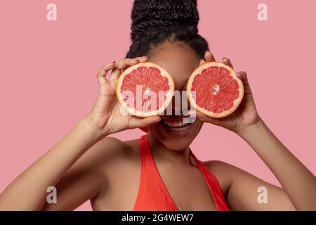 Dunkelhäutige Frau, die Grapefruitscheiben hält und glücklich aussieht Stockfoto