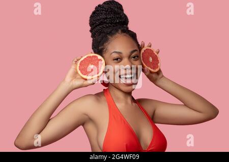 Dunkelhäutige Frau, die Grapefruitscheiben hält und glücklich aussieht Stockfoto