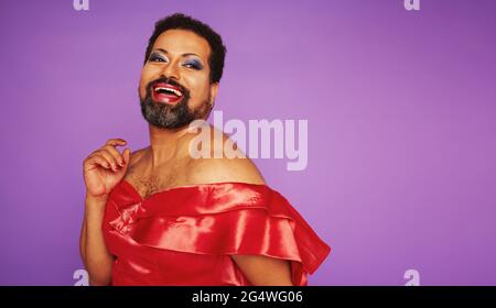 Porträt eines Genderqueers in glänzendem weiblichem Outfit. Ziehen Sie Königin in schönen Kleid und Make-up auf farbigen Hintergrund mit Copy Space. Stockfoto