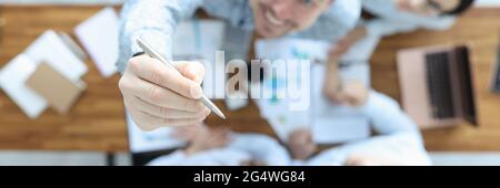 Eine Gruppe von Geschäftsleuten sitzt am Tisch von oben. Mann zeigt den Stift nach oben Stockfoto