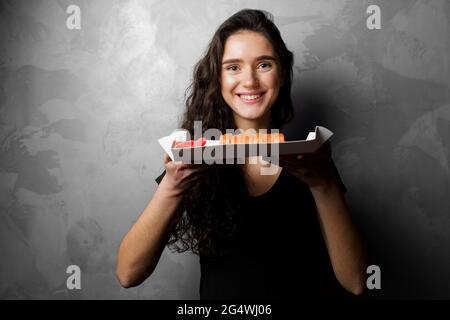 Mädchen hält philadelphia Rollen in einem Papierkarton auf grauem Hintergrund. Sushi, Lieferung von Lebensmitteln Stockfoto