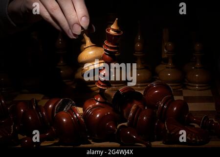 Weibliche Hand spielen Schach und schlagen den König auf einem dunklen Hintergrund. Altes Schach. Business-Konzept Stockfoto
