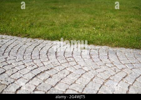 Gefliester Gehweg in der Nähe von grünem Rasen, geringe Schärfentiefe, abstraktes Photon, nur wenige Steinfliesen im Fokus Stockfoto