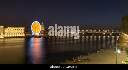 Eine ikonische Landschaft mit einem Riesenrad, einer Brücke und den nächtlichen öffentlichen Zusammenkünften am Fluss Garonne in Toulouse, Frankreich. Stockfoto