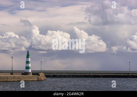 Ein grüner Leuchtturm in Nida am Hafen der Kurischen Lagune. Ein Vogel auf der Oberseite und Wolken im Hintergrund. Stockfoto