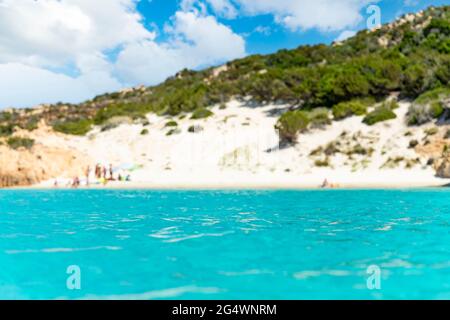 (Selektiver Fokus) Unschärfe-weißer Sandstrand im Hintergrund, der von einem wunderschönen türkisfarbenen Meer im Vordergrund gebadet wird. Stockfoto