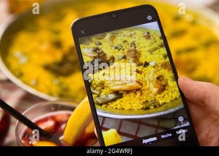 Bild eines Fotografen, der eine typische Paella in einem Restaurant in Valencia fotografiert und dabei ein Glas Sangria mit Rotwein verkostet Stockfoto