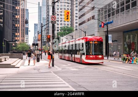 TORONTO, KANADA - 06 05 2021: Fußgänger und Straßenbahn an der Kreuzung von King Street und Bay Street in der Innenstadt der größten kandianischen Stadt - Stockfoto