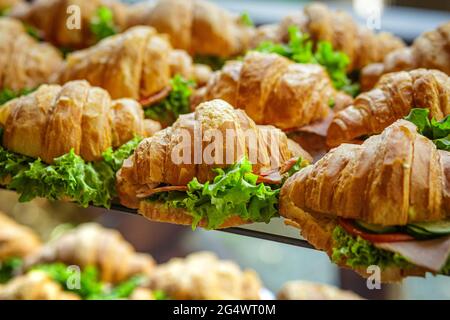 Sandwiches mit Croissants, Schinken, Tomaten und Salat. Viele leckere schnelle gesunde Lebensmittel. Snack bei der Veranstaltung. Stockfoto