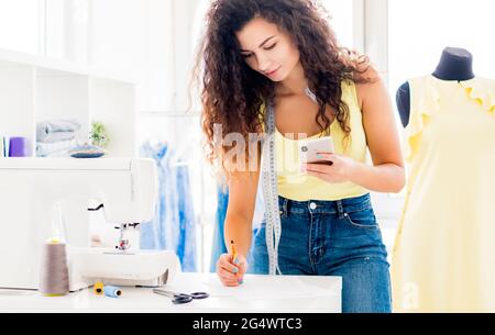 Glückliche Näherin telefoniert in der Nähwerkstatt Stockfoto