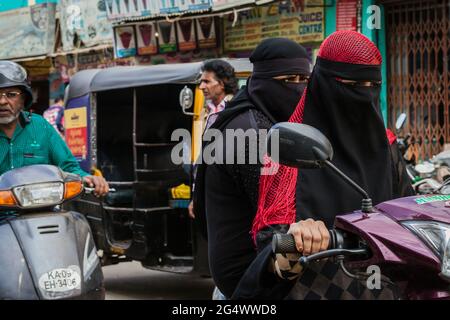 Zwei muslimische indische Frauen, die Niqab tragen, reiten mit dem Motorrad auf der belebten Straße, Mysore, Karnataka, Indien Stockfoto