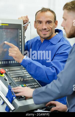 Ingenieur, der Lehrlinge für den Einsatz computergestützter Bearbeitungsmaschinen unterrichtet Stockfoto