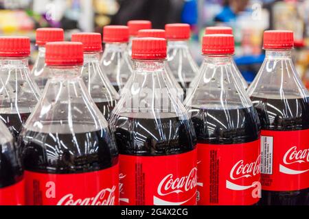 Koksflaschen. Mehrere Flaschen Coca-Cola-Klassiker Reihen sich in ordentlichen Reihen an. Die klaren Flaschen enthalten dunkelbraune Soda mit roten Etiketten und Verschlüssen. Stockfoto