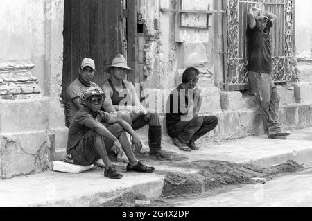 Kubanische Bauarbeiter sitzen gemächlich vor einem alten, teilweise beschädigten Gebäude mit etwas Bausand vorne. Stockfoto