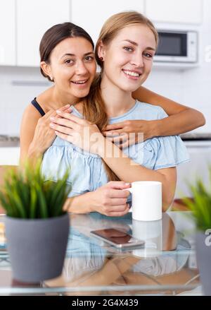 Junge lächelnde emotionale Freundinnen umarmen und Spaß am Tisch haben Stockfoto