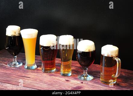 Sechs Gläser mit verschiedenen Biersorten stehen auf einem Holztisch in einer Reihe. Seitenansicht. Stockfoto