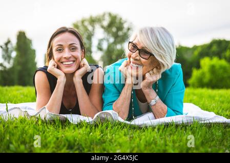 Lächelnde Frauen mit Händen am Kinn auf der Picknickdecke Stockfoto