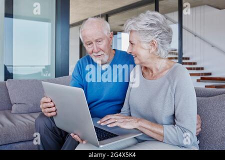 Ein Seniorenpaar mit Laptop sitzt auf dem Sofa im Wohnzimmer Stockfoto