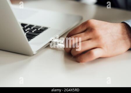 Geschäftsmann, der den USB-Stick in den Laptop auf den Schreibtisch steckt Stockfoto