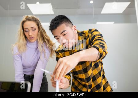 Junger Profi, der die Windenergieanlage anpasst, während er neben einer Kollegin im Büro steht Stockfoto