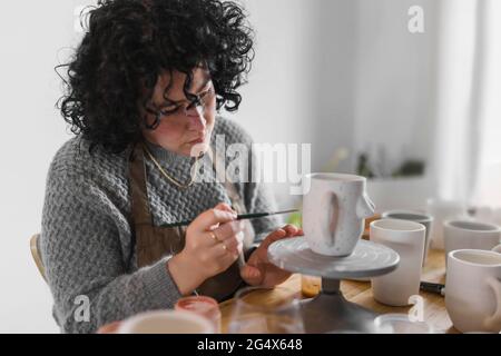 Expertin mit Pinsel, die am Arbeitsplatz an einem Keramikbecher arbeitet Stockfoto