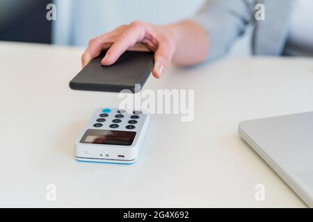 Weibliches professionelles Scan-Mobiltelefon mit Kartenterminal am Schreibtisch Stockfoto