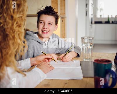 Sohn lächelt, während sie zu Hause bei der Mutter studiert Stockfoto