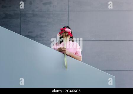 Frau, die am Geländer einen Haufen Gerbera-Gänseblümchen vor dem Gesicht hält Stockfoto