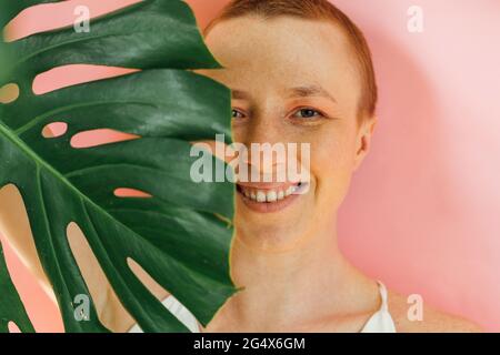 Das Gesicht der lächelnden Frau ist mit einem grünen Blatt bedeckt Stockfoto